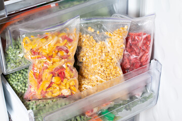 Plastic bags with different frozen vegetables in refrigerator.