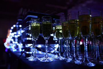 Beautifully glowing champagne glasses on the table against the backdrop of a festive atmosphere with neon illumination.