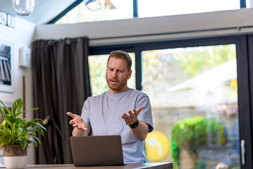 Portrait of a worried angry young adult man having video call or online conference on laptop computer arguing, fighting and shouting on coworkers and colleagues. Bad news reaction.