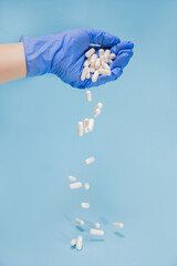 White tablets and capsules fall from the doctor's hand in a blue glove on a light blue background in the form of a frame with a place for text. Pharmaceutical, Covid-19 or coronavirus. Vertical image