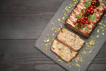 Traditional French terrine covered with bacon on dark wooden background with Christmas decorations