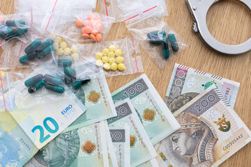 On the table lies currency in banknotes of different countries and drugs in pills and handcuffs.