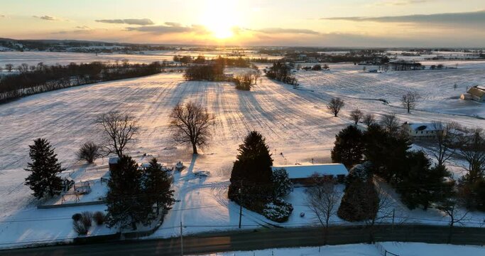 Rural farmland in winter snow. Sunset with family homes farm barns. Agriculture in USA theme. Scenic aerial truck shot.