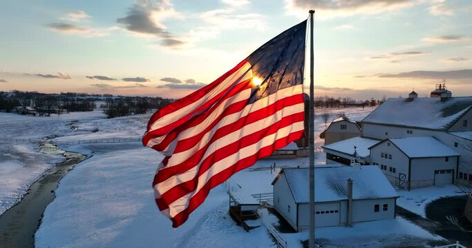 Cinematic slow motion American flag. USA pride in rural winter farm scene. Aerial starburst effect at sunset.