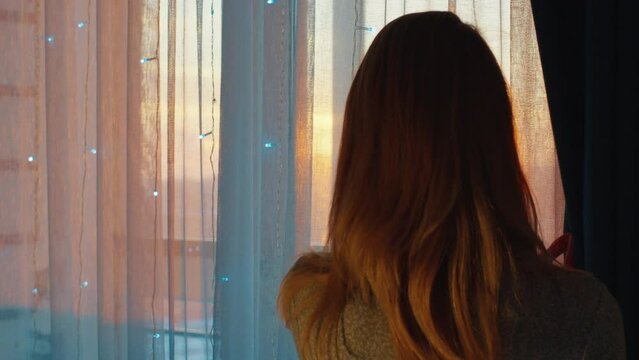 Young woman watches sunset trough the window