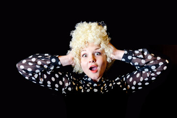 Curly girl - blonde in a blouse with polka dots like a clown screams on a black background