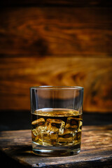 Glass chilled whiskey with ice cubes on wooden background in cellar.