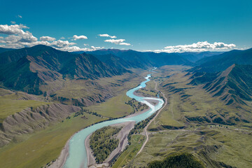 Azure mountainous valley from copter with a narrow river flowing under a bright blue sky with several clouds.