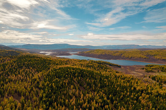An image taken from a bird's-eye view of green and yellow trees, a deep river and mountains in the distance.
