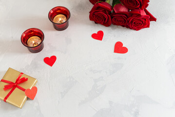 Romantic background with product place or copy space. Red roses bouquet, gift boxes, small hearts and candles on light concrete background. Romantic love background. Happy Valentine's Day.