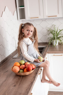 cute little girl at home in the kitchen with fruits, eating red and green apples, oranges. growth and development of children. Healthy food, natural vitamins, baby dieting concept. selective focus