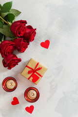St. Valentine's Day background. Small hearts, candles, a gift box and red roses bouquet on light concrete background. Romantic love background. Happy Valentines Day. Greeting card, poster. Top view