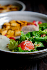 Traditional caesar salad in a white bowl on a old dark rustic table. Selected focus.
