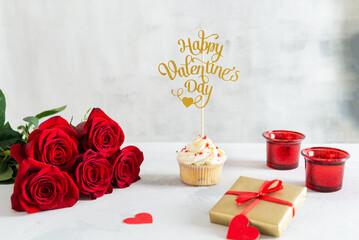 Romantic gift for Valentine's Day. Cupcake with vanilla cream and red sugar hearts and roses bouquet with a gift on light background. Recipe. Bakery, confectionery menu, greeting card. Copy space