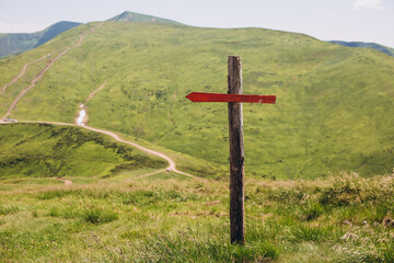 One wooden red signpost in the summer mountain with copyspace. Conceptual leading indicator. Old Arrow on the wooden signpost pointing to a direction.