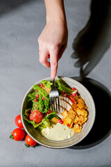 Traditional caesar salad in a white bowl on a dark gray table background. Selected focus.