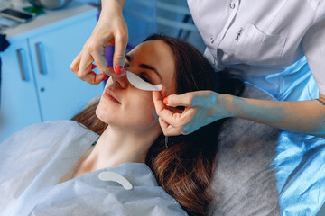 The cosmetologist applies eye patches providing a beauty service to a young client lying in a chair.