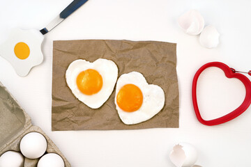 Heart shaped fried eggs served on craft paper, white background, flat lay, top view.
Valentines day breakfast idea. 