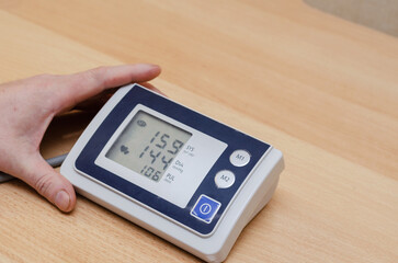 A man's hand holds a digital blood pressure monitor on the table