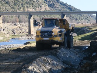 Engin de chantier de travaux camion benne et grue le long d'une berge rivière