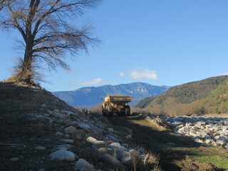 Fototapeta premium Engin de chantier de travaux camion benne et grue le long d'une berge rivière