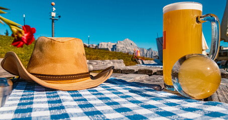 Crystal ball alpine summer landscape shot with a cowboy hat and a glass of beer on a wooden table at the famous Asitz summit, Leogang, Salzburg, Austria