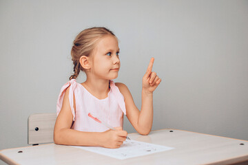 Portrait of a smart beautiful young model sitting at a table with a sheet of cursive paper and pointing her finger up. Here can be your advertising. photo with noise