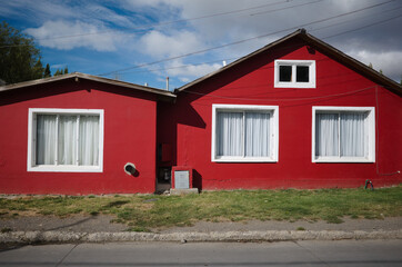 Fototapeta na wymiar One-story house with red facade, white windows and white curtains on windows along street. Small private house in El Calafate, Patagonia, Argentina. Typical building in Argentinian part of Patagonia