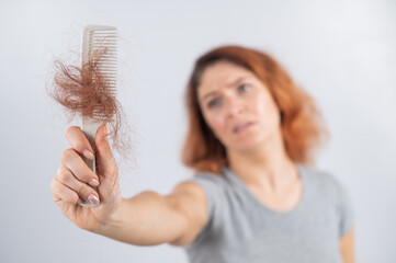 Caucasian woman with a grimace of horror holds a comb with a bun of hair. Hair loss and female...