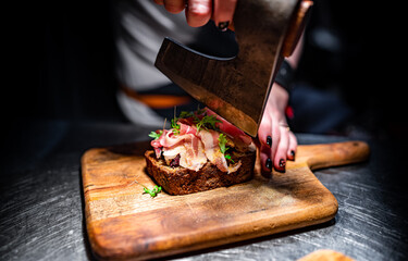 Woman chef hand cutting tasty sandwich with axe on wooden plate