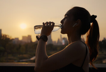 Young woman drinking water after jogging at sunset.