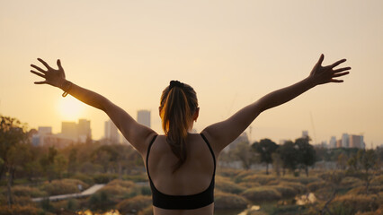 Young woman outstretched arms and standing in the city at sunset.