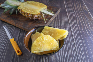 Fresh pineapple halved with pineapple slices in bowl on wooden table