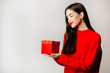 The girl is looking down at her present box. The gift is covered in a red box. Beautiful girl looks happy. Concept of St. Valentine's Day