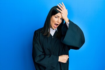 Young hispanic woman wearing judge uniform surprised with hand on head for mistake, remember error....