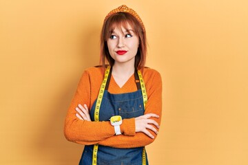 Redhead young woman dressmaker designer wearing atelier apron smiling looking to the side and staring away thinking.