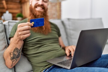 Young redhead man using laptop and credit card at home
