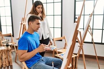 Student and teacher with serious expression painting at art school.