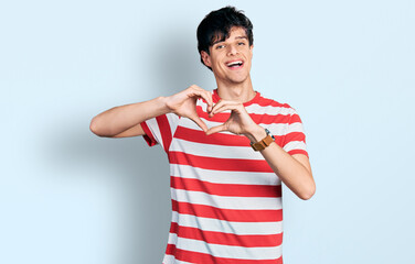 Handsome hipster young man wearing casual striped t shirt smiling in love doing heart symbol shape with hands. romantic concept.