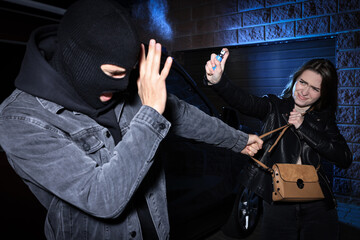 Fototapeta na wymiar Woman using pepper spray while thief trying to steal her bag outdoors at night. Self defense concept