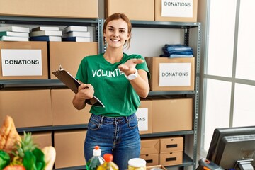 Young brunette woman wearing volunteer t shirt at donations stand smiling cheerful offering palm...