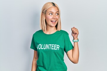 Beautiful blonde woman wearing volunteer t shirt smiling with happy face looking and pointing to...