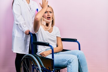 Beautiful blonde woman sitting on wheelchair with collar neck surprised with hand on head for...