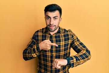 Young hispanic man wearing casual clothes in hurry pointing to watch time, impatience, upset and angry for deadline delay