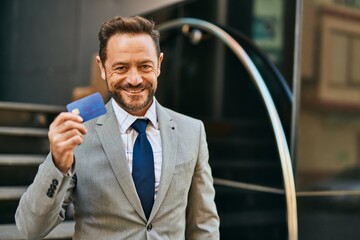 Middle age businessman smiling happy holding credit card at the city.