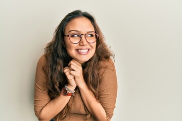 Young hispanic girl wearing casual clothes and glasses laughing nervous and excited with hands on...