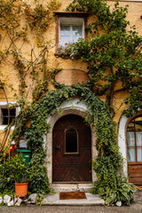 Fototapeta na wymiar Hallstatt, Austria, 27 August 2021: Colorful scenic picturesque town street at summer day, oval wooden door, braided window, green ivy at yellow wall, traditional historical house, village near lake