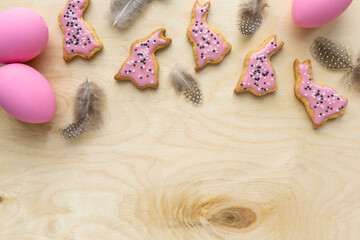 Homemade easter cookies in the shape of bunnies with feathers and eggs on wooden background, space for text
