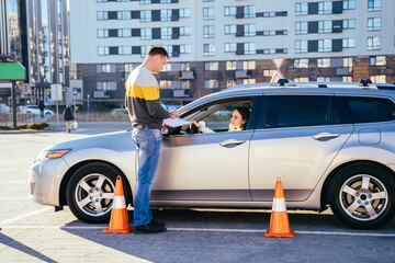 Man instructor standing outside of car and teaching his female student how parking car correctly.