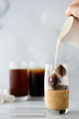 pouring milk into a glass of iced espresso